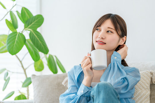 A woman relaxing on her sofa at home, sipping coffee and a hot drink.