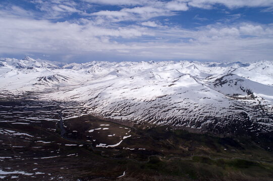 Aerial view of the snow-capped peaks of Babusar Top with a winding road through the valley and patches of snow in Naran, Khyber Pakhtunkhwa, Pakistan.