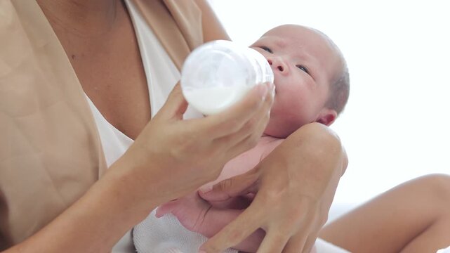 Close up of a mother bottle feeding formula or breast milk to her cute newborn baby boy or girl. Infancy healthcare, nutritious food, and parenting lifestyle concept.