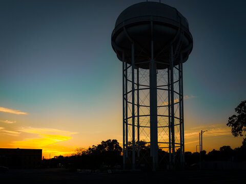 Tall metal water tower silhouette standing against a colorful sunset sky in an industrial area