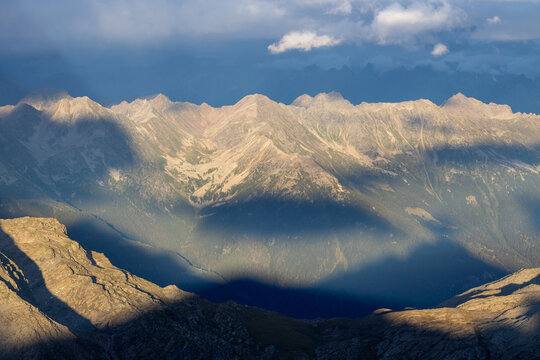 View of the rugged mountain peaks of the Alps with dramatic shadows cast across the rocky slopes under a clear sky in Valmalenco, Lombardia, Italy.