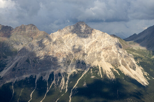 View of the rugged rocky peaks of the Alps under a dramatic cloudy sky with deep shadows cast across the slopes, Valmalenco, Lombardia, Italy.
