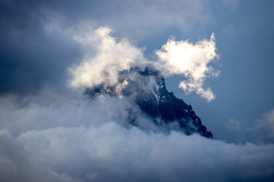 View of the Massiccio del Monte Bianco peak partially obscured by thick clouds and mist in the alpine landscape of Valle d'Aosta, Italy.