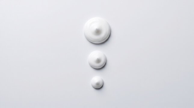 Three dollops of white cosmetic cream of different sizes arranged vertically isolated on white background