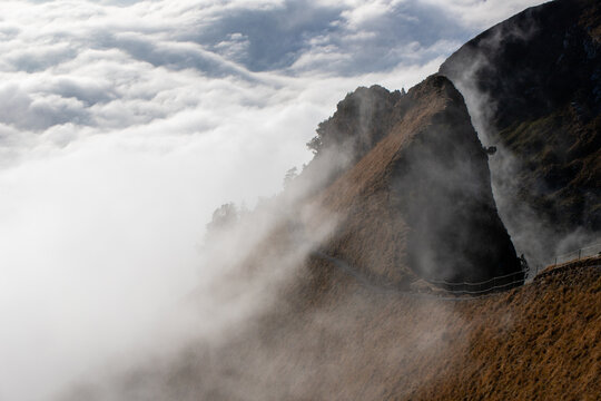View of the Stoos mountain ridge partially shrouded in mist with a narrow hiking path winding along the steep slope in Morschach, Schwyz, Switzerland.