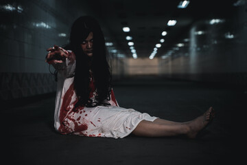Halloween theme featuring scary woman sitting on floor wearing bloody white gown inside dark corridor reaching hand forward during horror night celebration event activity © sorapop
