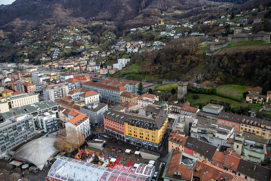 View of the historic Castles of Bellinzona overlooking the urban rooftops, streets, and a seasonal ice rink in the city center of Bellinzona, Ticino, Switzerland.