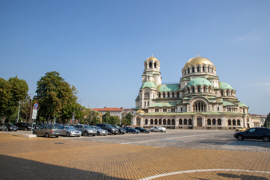 View of the Alexander Nevsky Cathedral with its iconic golden domes and green roof, set against a clear blue sky in a cobblestone square in Sofia, Sofia City Province, Bulgaria.