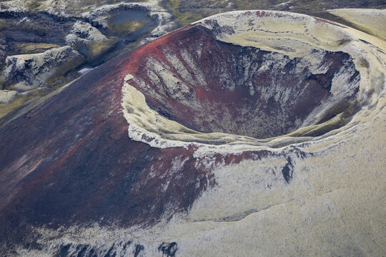 View of a volcanic crater with reddish-brown rock and moss-covered slopes in the rugged landscape of Iceland.