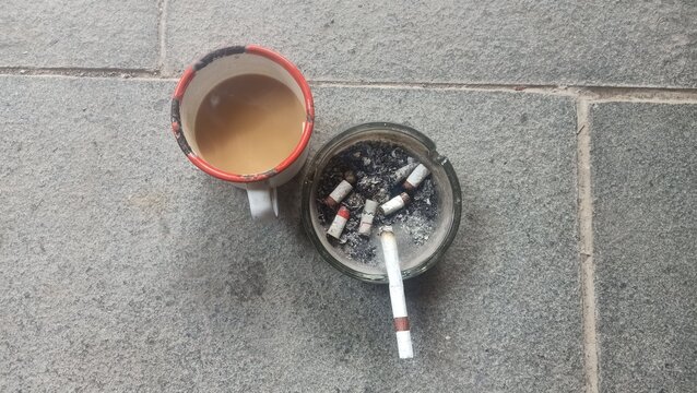 Top View of Coffee Mug and Glass Ashtray with Cigarette Butts on Stone Floor