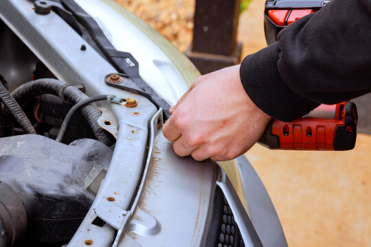 Car mechanic worker is repairing car engine in driveway with tools in hand parts open.