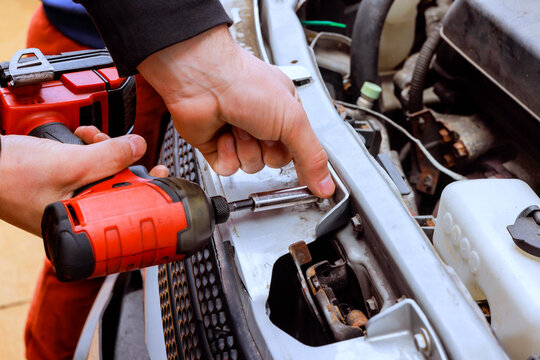 Mechanic uses power drill to work on car engine in garage tools are nearby engine parts