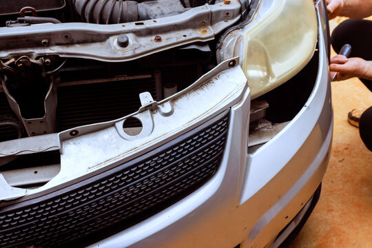 Worker repairing front part of damaged car in an automotive garage,