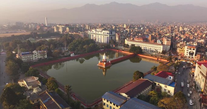 Kathmandu, Nepal, high-angle aerial shot of Ranipokhari artificial pond and central Balgopaleshwor temple, and surrounding urban traffic, the Dharahara tower with slight visible mountain range in back