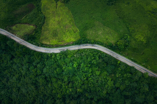 Top-down aerial view of a winding road going through dense green forest and mountain landscape.