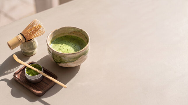Minimalist commercial setup of ceremonial matcha tea preparation with a ceramic bowl, bamboo whisk and powder on a beige microcement table
