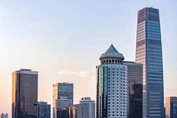 Fototapeta premium A cluster of modern high-rise buildings forms a dense urban skyline under a pale dawn sky, showcasing contemporary architectural design.