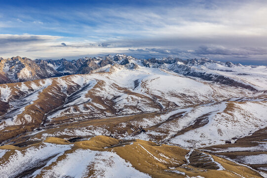 Aerial view of snow-dusted mountain ranges and open high plateau under a partly cloudy sky.