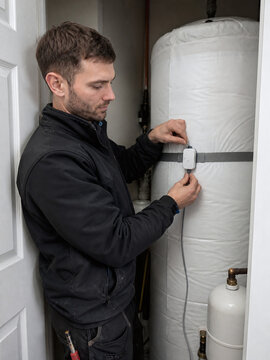 Technician installing a strap-on cylinder thermostat on a domestic water tank
