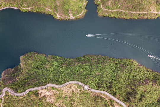 Aerial shot shows two boats moving on a dark river, surrounded by green vegetated land and winding paths.