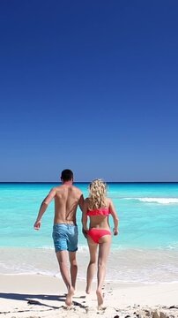 Young couple running in to the ocean on caribbean beach. Tropical vacation. Travel destination. Vertical footage
