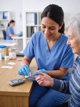 Caring nurse performing a blood glucose test on an elderly patient in a clinic