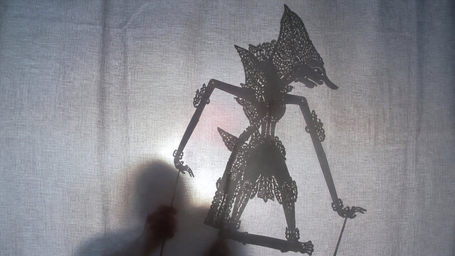 Traditional wayang kulit shadow puppet performance behind lit cloth screen