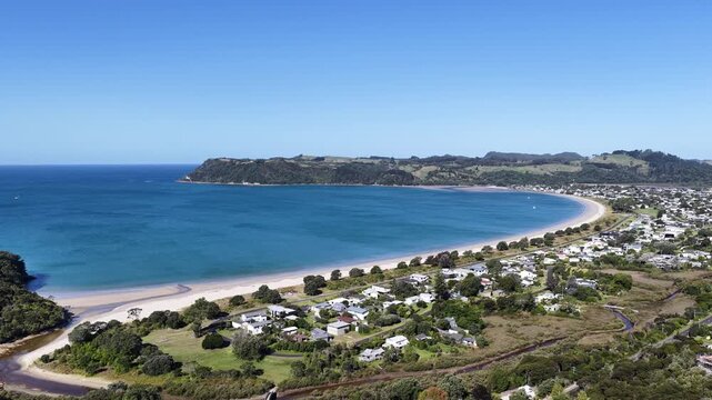 New Zealand aerial drone view of coastal bay beach pull back turquoise water green headland town landscape, drone moves backward over.