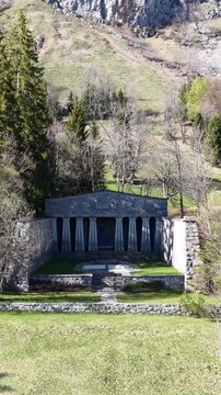 Stone memorial with columns and enclosed courtyard stands on a grassy wooded hillside in Switzerland.