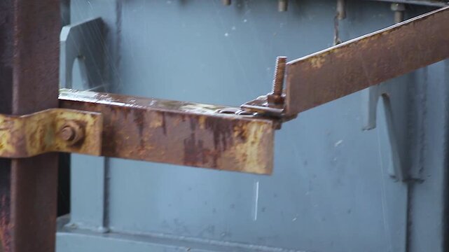 Rusted steel hinge closeup shows weathered bolts and joint on industrial equipment, texture of corrosion and aged metal.
