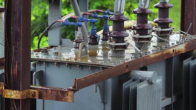 Power transformer close up with ceramic insulators and wires wet from rain, electrical substation equipment, industrial energy infrastructure detail shot.
