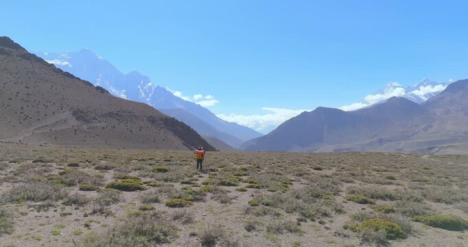 Annapurna Circuit, Mustang Nepal, drone pull-out shot of a lone backpacker holding a map and walking in a vast, dry Himalayan desert valley.