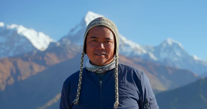 Annapurna region, Nepal, Portrait shot of a local ethnic Gurung Himalayan porter guide wearing a woolen beanie hat with the snow-covered peak of Annapurna South in the backdrop.