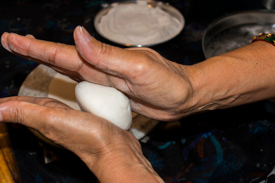 hands rolling dough ball with both hands while preparing homemade chapati at indian kitchen