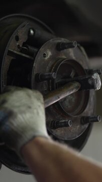 Mechanic uses a hammer to hit car wheel hub assembly.