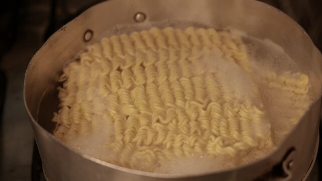 Close-up of instant noodles cooking in a pot. Noodles boiling in a pot on the stove. Pasta cooking in a pot of hot water. POV: making instant ramen in the kitchen; preparing macaroni. Steam rising 