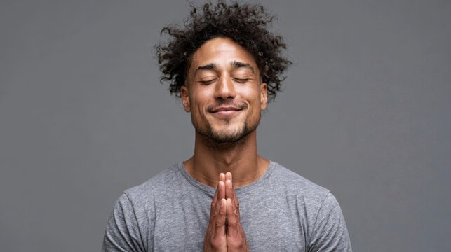 Young man with curly dark hair and tan skin praying with hands together in a moment of gratitude