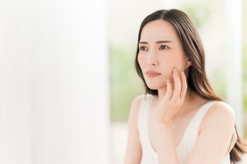 Naklejka premium 鏡を見ながら肌をチェックする日本人女性。スキンケアイメージ。