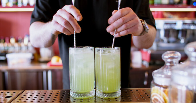 Preparing beverage. Pub service. Male barkeeper hand mixing cold green pistachio syrup cocktail with sparkling water spoon in glass.