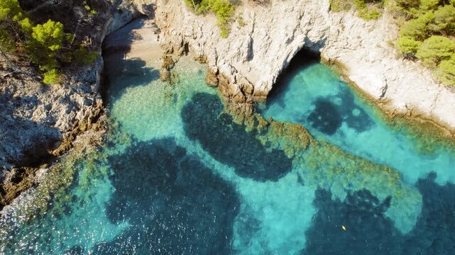 Aerial view of a rocky cove with clear blue water and hidden beach in Kefalonia