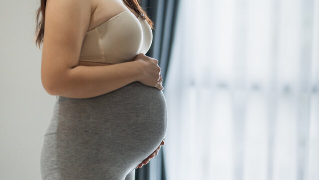Pregnant woman gently holding her baby bump at home, expressing maternal care and anticipation.