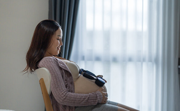 Happy pregnant woman listening to music with headphones on her baby bump at home.