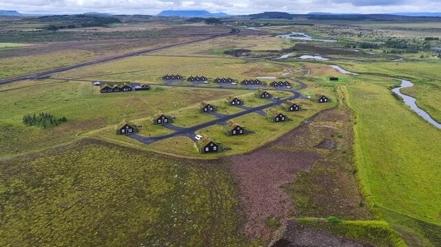 Aerial view of traditional dark cabins with grass roofs set in the vast green landscape of Selfoss, Sveitarfelagid Arborg, Iceland.