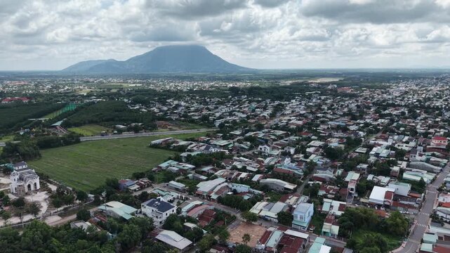 Wide aerial tracking sideways above a Tay Ninh town, a highway cutting through the rooftops with Ba Den Mountain rising beyond the plain, Vietnam.