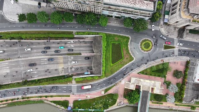 Top down aerial holding steady above a road underpass and small roundabout, cars and motorbikes streaming through the junction on both levels, Ho Chi Minh City, Vietnam.