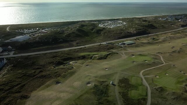 Drone flight over greens and bunkers of the links course at Hornum on Sylt towards the coastal road, the campsite and the shining North Sea