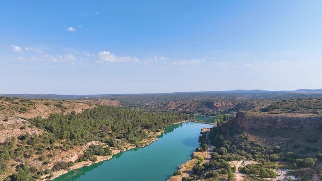 Aerial traverses the surrounding hills and central long gorgeous lagoons of the Lagunas de Ruidera complex under a warm, blue sky. Spain.