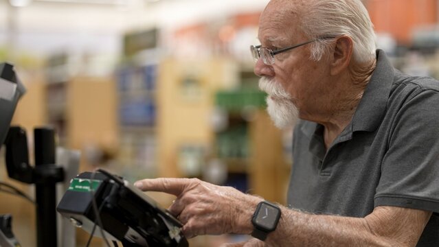 An elderly man is at the self-checkout in a grocery store checking items and completing his shopping