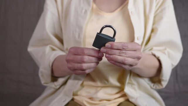Woman's hands opening padlock with a key. Person sitting on a sofa and holding a padlock in their hands, then opening the lock with one of the keys on a ring, representing concepts of access, security