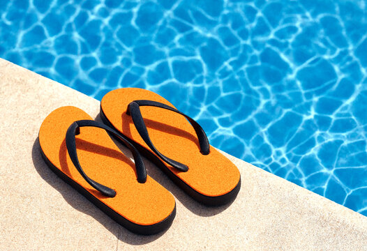 Bright orange flip flops resting on the edge of a sparkling blue swimming pool on a sunny day